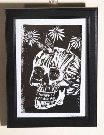 Black and white print of a skull, turned slightly to the left with daisies growing out of the skull