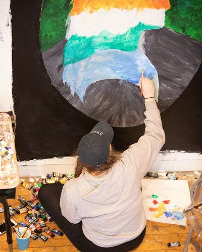 Student painting a large, colorful, self-portrait