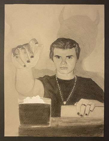A teenage boy holds a hand over a lit candle. His shadow has two pointed horns, and he wears all black. In his other hand is a book and rosary beads.