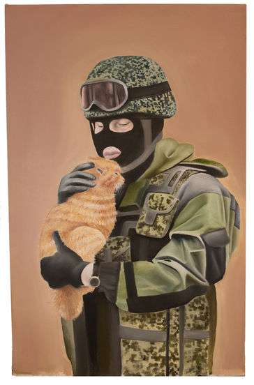 A man dressed in camouflage, cradling an orange and white cat lovingly. 
