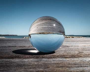 A glass ball on a wooden platform overlooking a beach. The beach is depicted upside down in the glass ball
