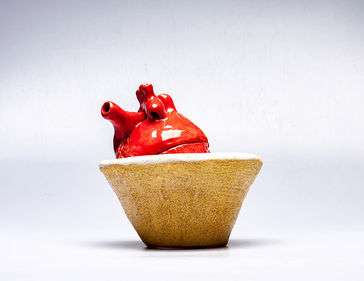 ceramic anatomical heart with the top hat being a lid. Resting on a ceramic cone shaped base resembling sand