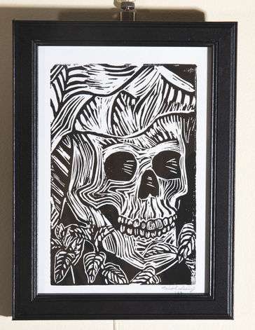 Black and white print of a skull with a witch hat surrounded by a bed of mint.